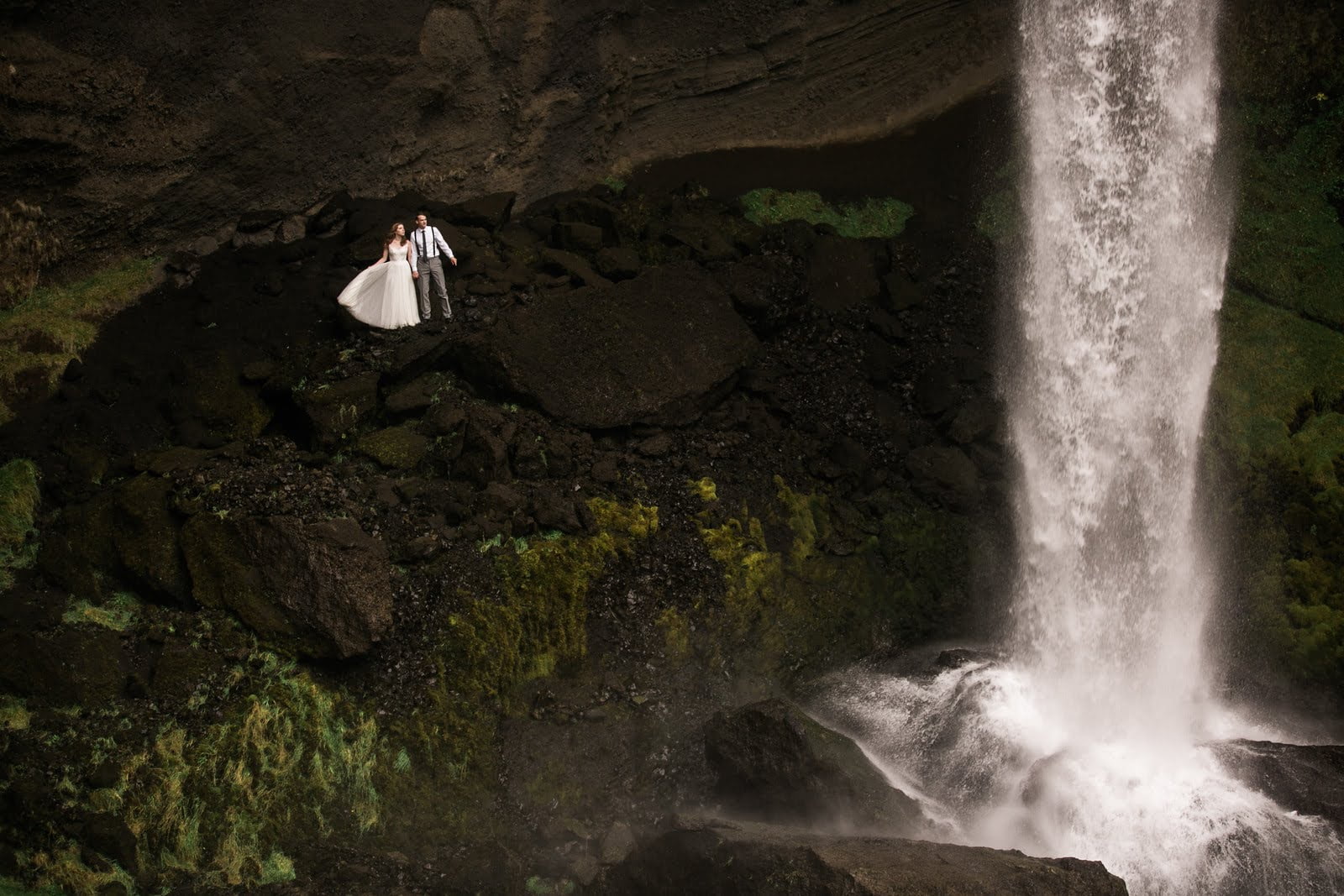 Meredith and Joe join hands behind a waterfall during their Iceland Adventure Elopement