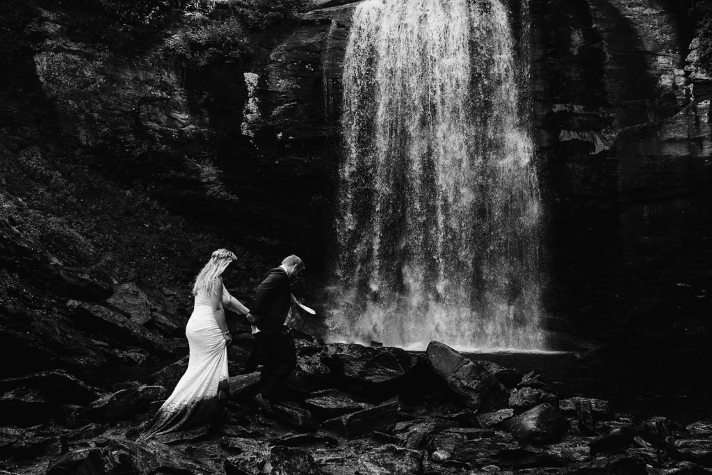 Travis leads Emily by the hand as walk toward a waterfall of the Blue Ridge Parkway on their Asheville Wedding day as photographed by Wilder Weddings Collective