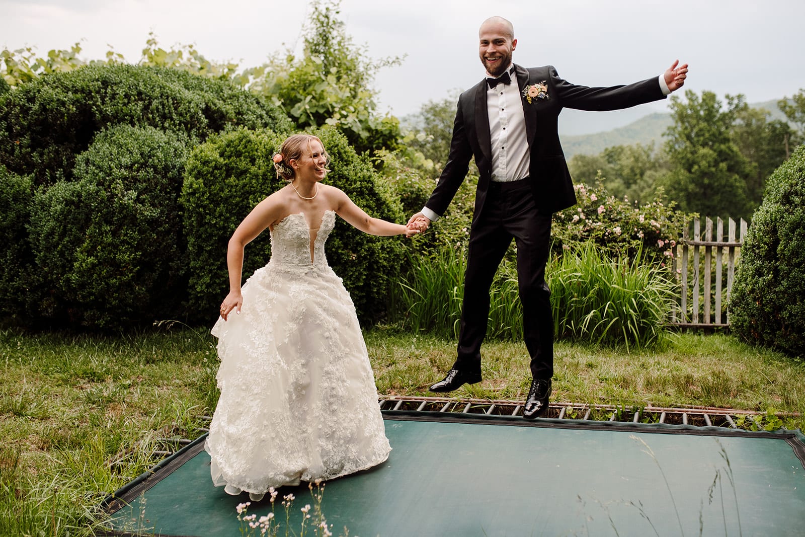 Kira+Jordan jump on a trampoline in their wedding attire at Sherill's Inn in Fairview, NC