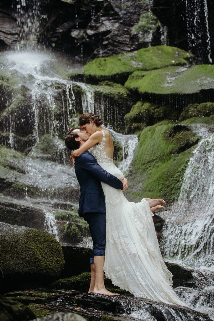 ali and mike share a kiss in front of a waterfall during their Asheville Adventure Elopement